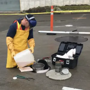 Urban worker in protective gear sampling wastewater near a manhole in a safe environment.