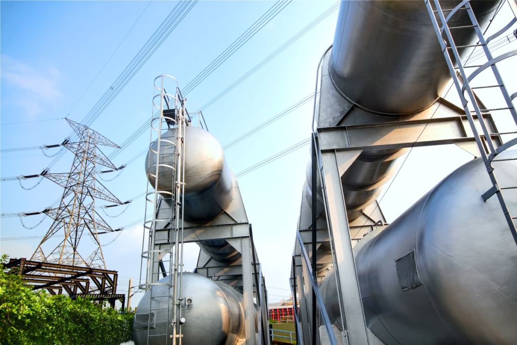 Industrial landscape featuring stainless steel tanks and electrical transmission tower under a blue sky.